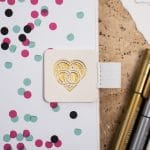 Stifthalter Stiftehalter Stiftschlaufe Pen Loop Extragroß Hochzeitsplaner Weiß - Befestigt auf einem Hochzeitsbuch. Brauner Hintergrund mit Hochzeitsplanung zu sehen. Zwei weiße Bleistifte mit goldener Gravur