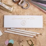 Weiße Bleistifte Set Hochzeit Hochzeitsplanung Gold Gravur Radiergummi - Geschenkeverpackung mit weißen Bleistiften 3 Stück liegt auf Tisch mit Hochzeitsdekoration, Wachssiegeln und Hochzeitsplanern